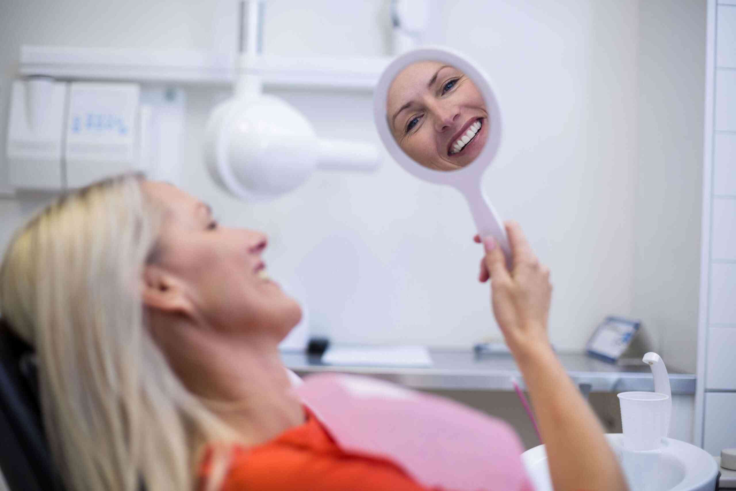 Patient smiling while checking teeth in a dental mirror after treatment.