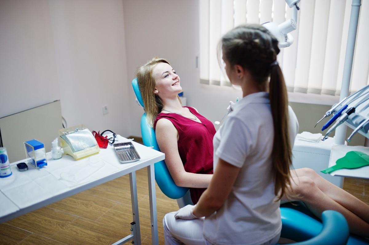 Patient sitting in dental chair speaking with dentist in clinic